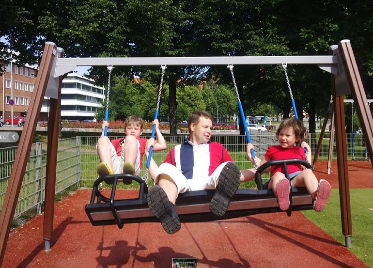 kuvassa  marko eskolainen keinuu kahden iloisen lapsen kanssa puistossa kesällä 