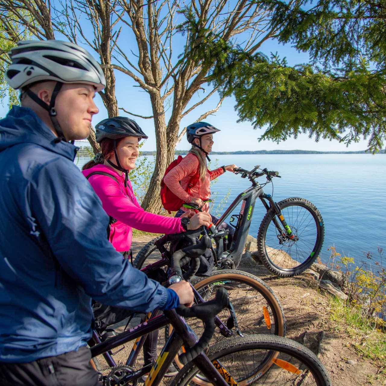Kolme pyöräilijää katsomassa järvimaisemaa.
